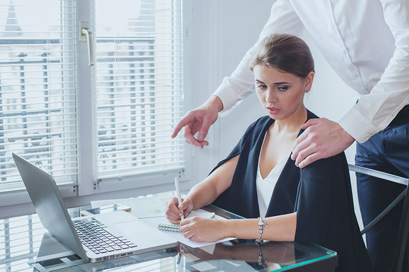 woman in office looking uncomfortably at boss's hand on her shoulder