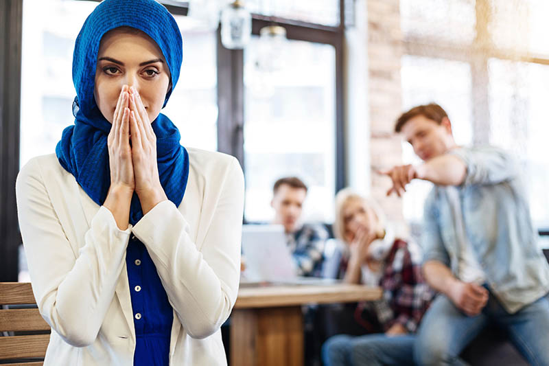 Muslim woman feeling humiliated as coworkers point in the background